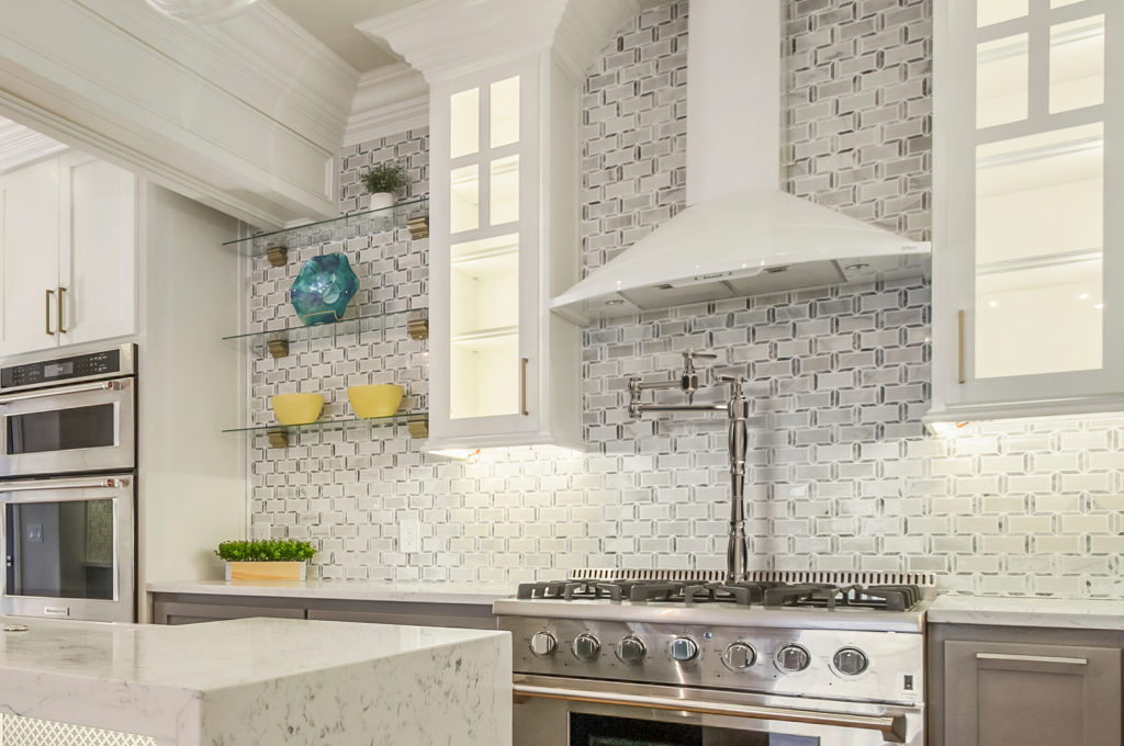 This kitchen design has a patterned backsplash with lit cabinetry. There is also some exposed shelving with yellow bowels, a blue vase and a green plant displayed.