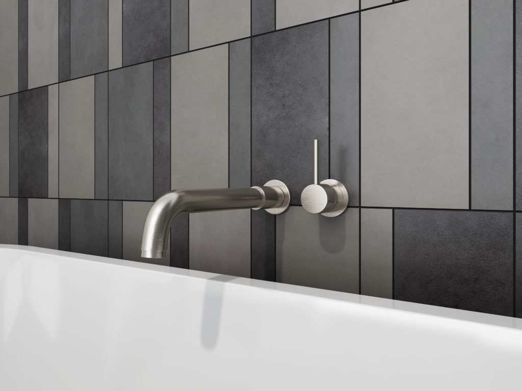 This wall-mounted bath faucet has a single temperature knob. The white tub is complimented by a dark, multi-colored tile siding.