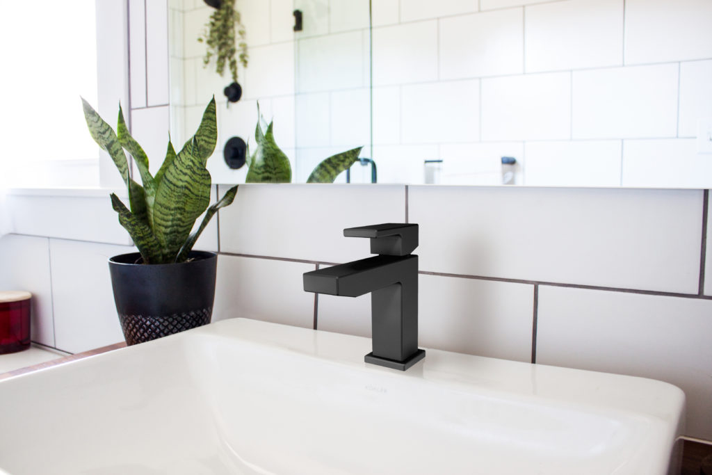 A matte black single-handed bathroom faucet with a white sink and subway tile backsplash.
