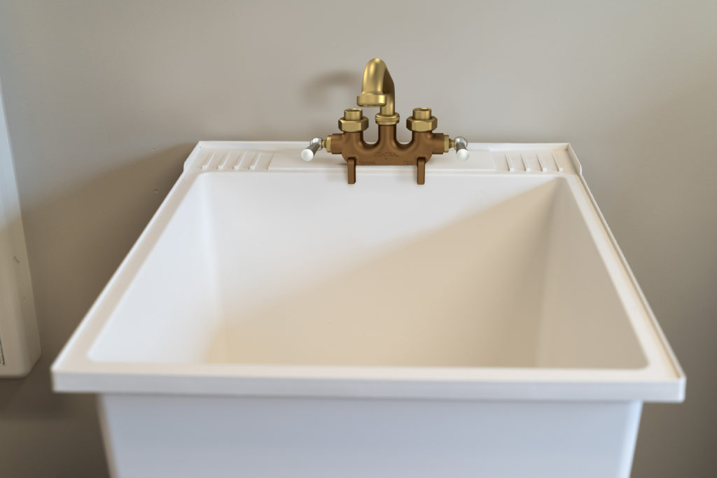  A white sink is mounted to a tan wall. There is exposed piping and silver fixtures.