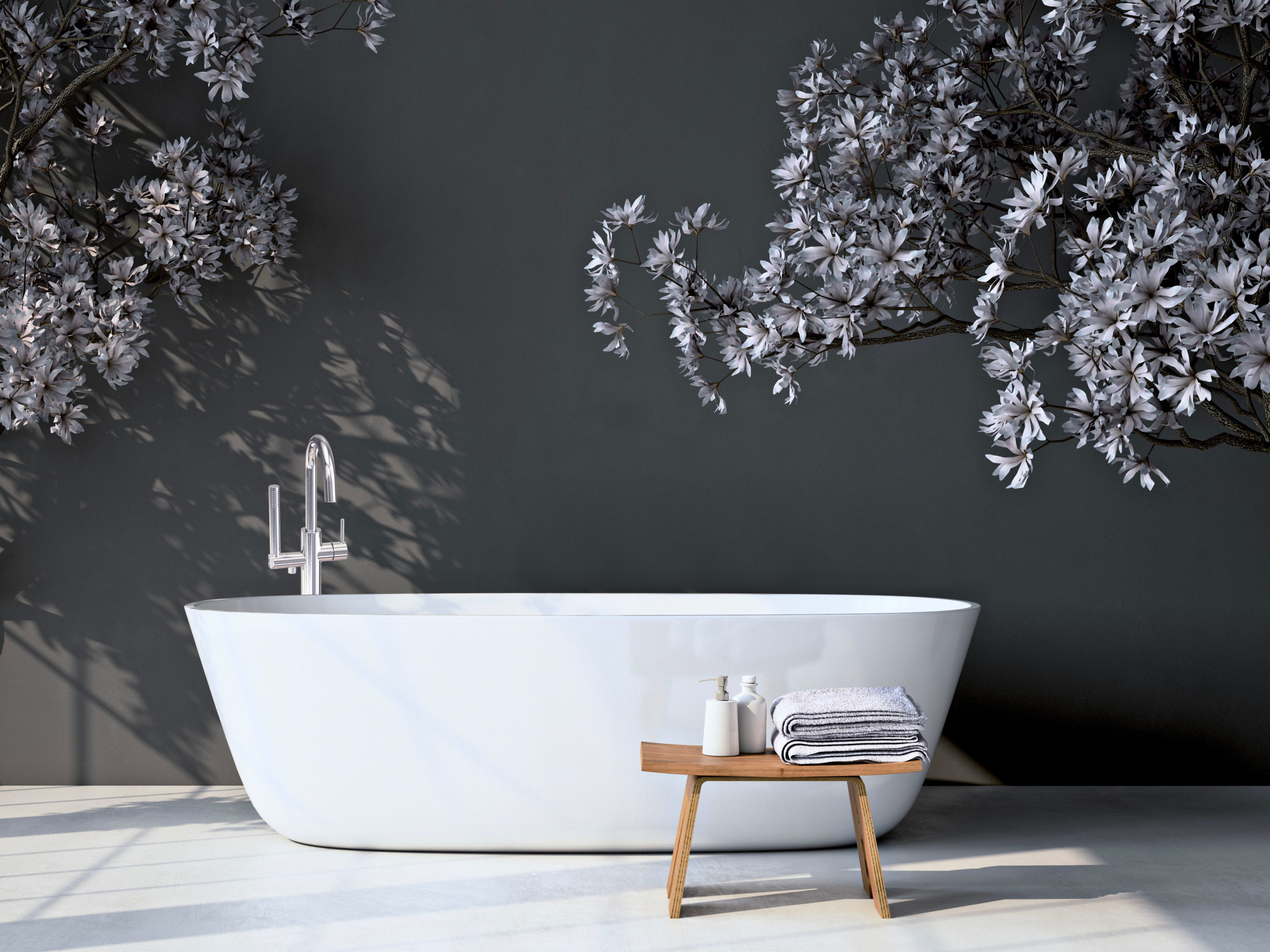 This bathroom has a white, freestanding tub with a silver faucet. There are trees featured in the space while a wooden stool is in front of the tub holding towels and bottles.