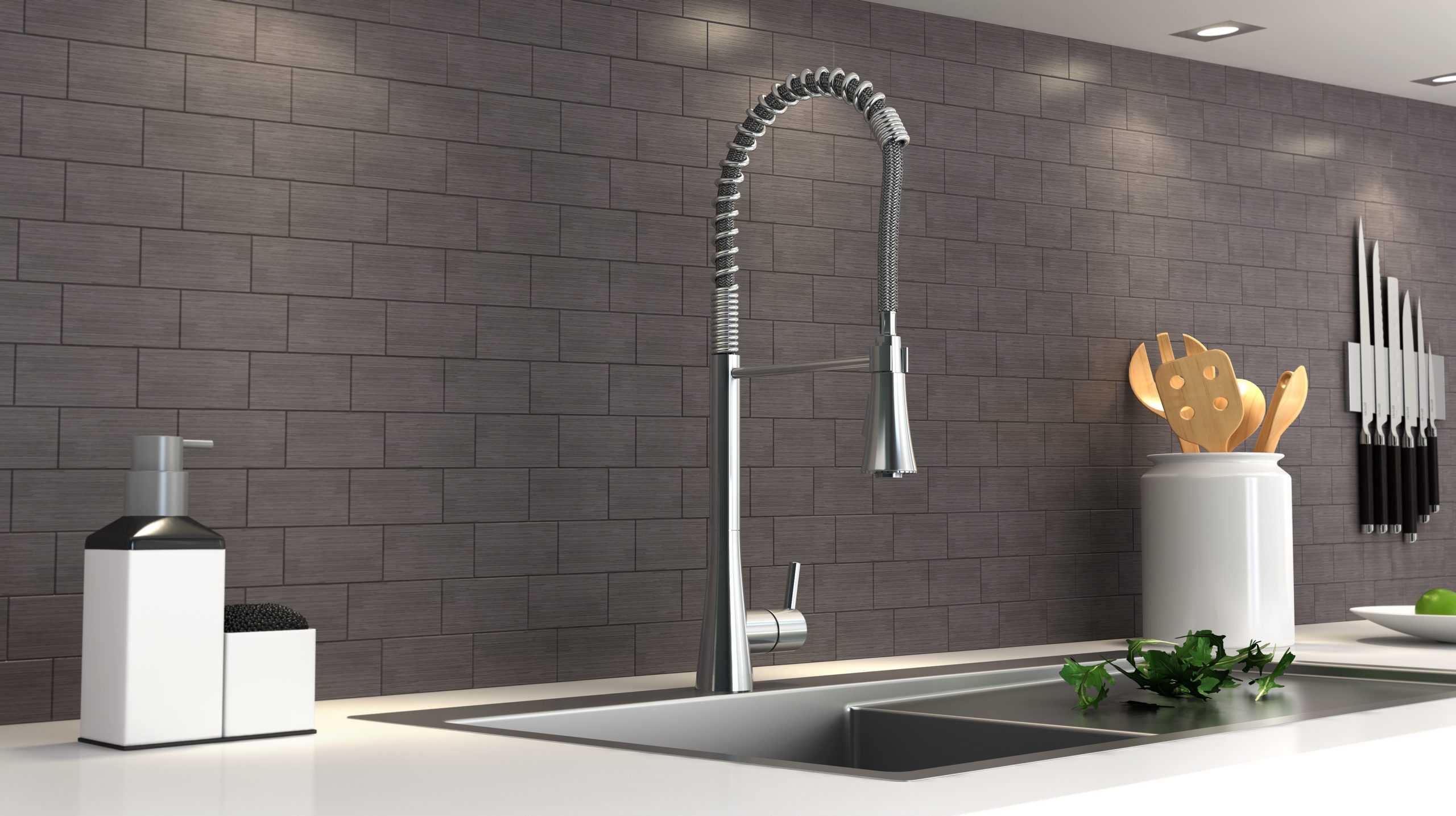 This kitchen design has a large, silver sink with a polished chrome finish. The counter has a soap dispenser, kitchen utensils and some lettuce displayed.