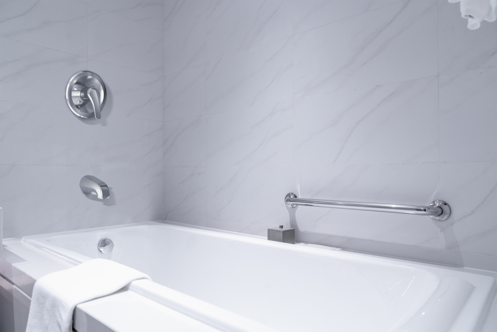 This white tub has marble siding with silver fixtures, including a shower bar. There is a white towel draped over the tub siding.