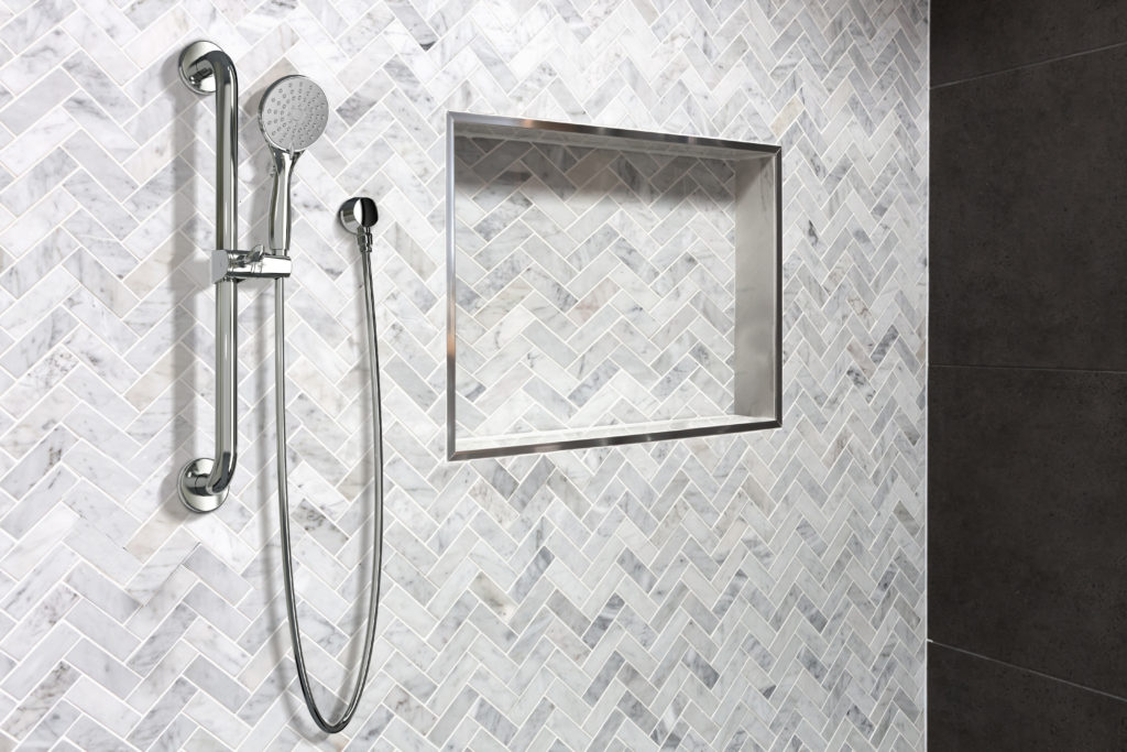 This shower design has a small, zig-zag tile design. The shower fixtures are silver, and there is a rectangle cut-out in the siding to make a shelf.