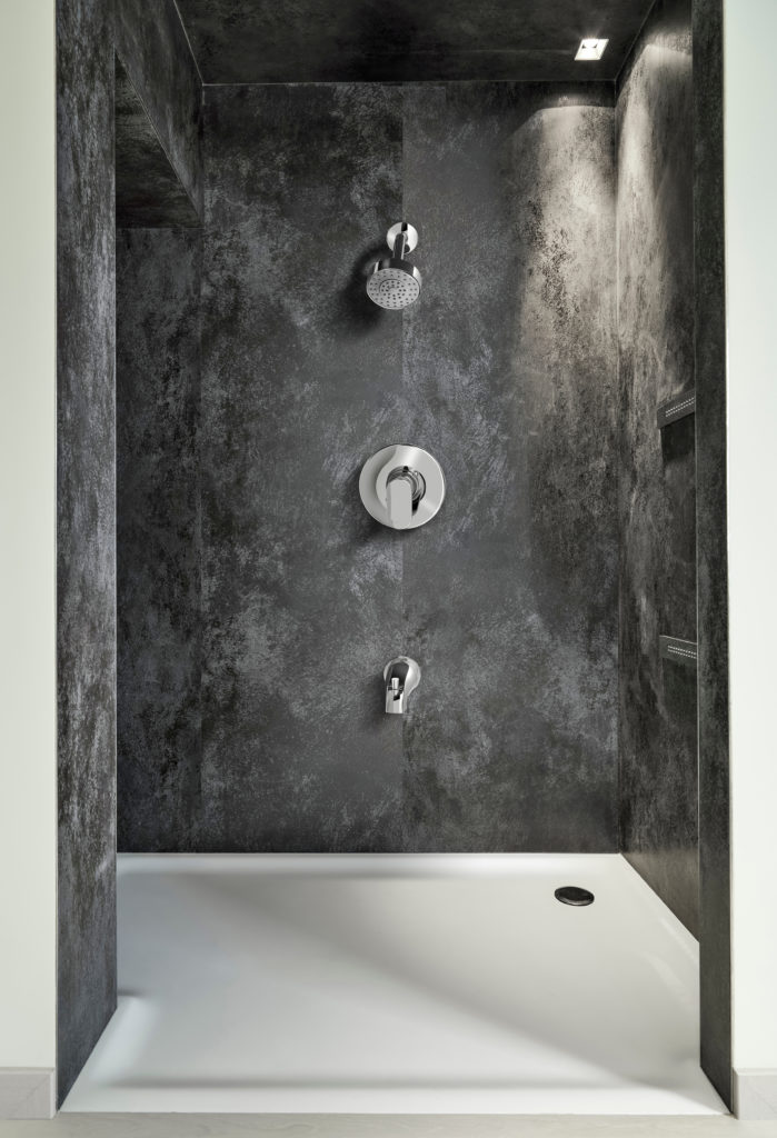 This walk-in shower has white flooring and dark marble siding. The fixtures are silver, and there is a light incorporated in the shower design.